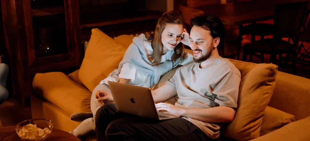 Par i sofa med computer bruger internet